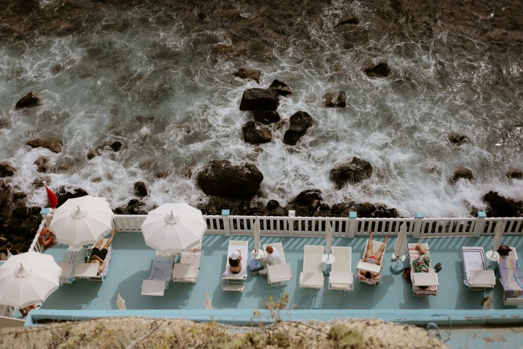 People relax by a pool near the rough sea.