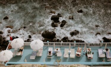 People relax by a pool near the rough sea.